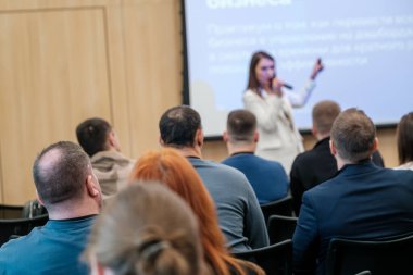 İş seminerinde konuşmacı dinleyicilere sesleniyor. Sunum sırasında dinleyen ve not alan katılımcılara odaklan.