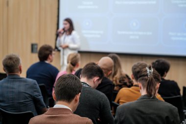 Konferans odasında projektör ekranıyla hoparlör dinleyen katılımcılar. Eğitim ve meslek ortamı.