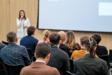 Modern bir konferans ortamında konuşmacı dinleyen seyircilerle iş semineri. Çeşitli katılımcılarla öğrenme ve ağ oluşturma üzerine odaklanmış sunum atmosferi.
