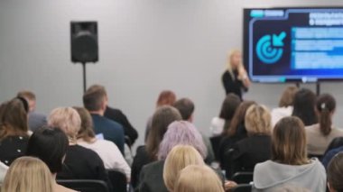 Katılımcılar, konuşmacı ve görsel slaytların yer aldığı iş konferansı sunumunda dikkatle dinliyorlar.