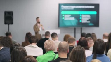 Teknik konferans konuşmacısı seyirciyi büyük ekranda sunumla meşgul ediyor. Modern mekan, odaklanmış dinleyiciler.