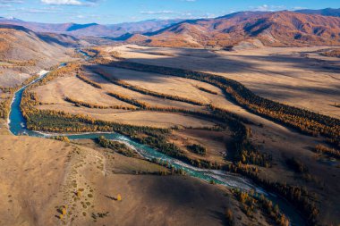 Aerial view of river meandering through autumn landscapes with golden trees and distant hills clipart