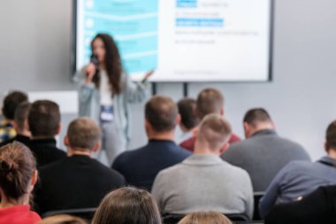 Kadın sunucu, iş konferansı sırasında izleyicileri öğrenme ve iletişim kurmaya yönlendiriyor. Profesyonel düzen ilham, fikir alışverişi, kariyer ilerlemesi ve işbirliği sağlar.