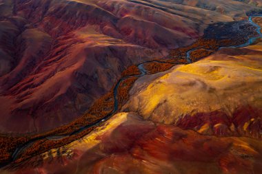 Aerial view showing an autumn-toned mountain landscape, vivid red colors, and a winding river. clipart