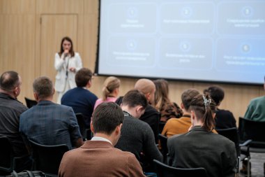 Dinleyiciler dikkatle modern bir ortamda iş konferansında konuşmacıları dinliyorlar..