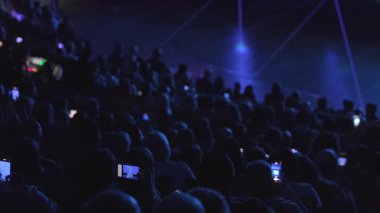 Büyük bir kalabalık tiyatroda oturmuş cep telefonlarıyla karanlık atmosferi aydınlatan parlayan ekranlarla sahneleri çekerken bir performans izliyordu.