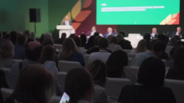 Konferansa katılanlar oturdular ve yeşil fon ile profesyonel mekanda sunucuyu dinlediler..