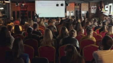 Modern bir konferans salonunda sunum dinleyen geniş bir grup insan.