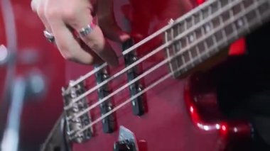 Yaylara odaklanmış basgitar çalan müzisyenlerin canlı görüntüsü. Enstrümanın canlı kırmızı yüzeyi tutkulu canlı müzik performansının sanatsal unsurlarını vurgular.