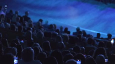 Kalabalık sahnede bir performansı dikkatle izlerken, pek çok kişi bu deneyimi akıllı telefonlarıyla kaydederek gözlemlenen gerçeklik ile paylaşılan medya arasında dinamik bir tezat oluşturuyor..