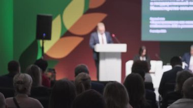 Modern ortamdaki konferansta profesyonel iş konuşmasında seyirciler dikkatle otururken.