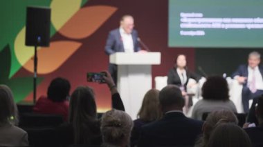 Konuşmacıyla konferans etkinliği sahnede, dinleyen katılımcılar ve renkli bir fon. Profesyonel bir ortamda temsil edilen iş ve iletişim kavramları.