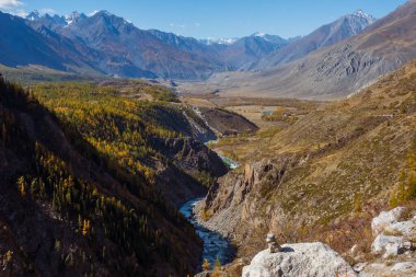 Sonbahar ormanı, dolambaçlı nehri ve mavi gökyüzünün altındaki uzak tepeleri olan dağ vadisi..
