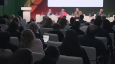 Profesyonel ortamda konuşmacıların yer aldığı bir panel tartışmasını izleyen konferans izleyicileri