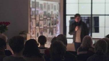 Konforlu bir odada, içinde fotoğraflar olan bir seyirciye sunum. İnsanlar sıcak ve davetkar bir ortamda hoparlöre dikkatle yaklaşır..