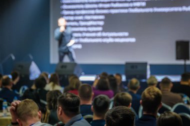 Büyük etkinlikte seyircilere arka planda bilgilendirme ekranı sunan konuşmacı.