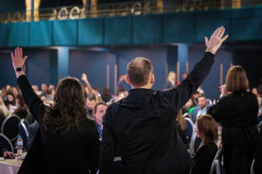 Bir grup birey, bir konferans ortamında bir iş etkinliği sırasında el kaldırdı