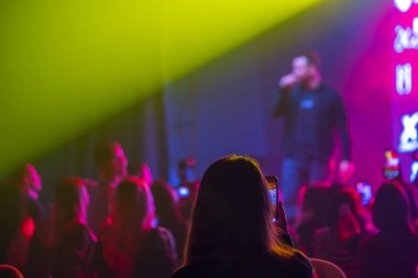 Seyirciler renkli konser ışıkları ve canlı atmosfer arasında akıllı telefonlardan canlı performans kaydediyorlar.