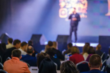 Profesyonel seminerde sahnede konuşmacı dinleyen seyircilerle iş sunumu.