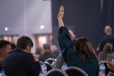 Seyirci, diğer katılımcıların arasında otururken konferans ortamında el kaldırır.