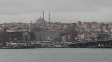 Gri gökyüzünün altında bir cami ve köprünün yer aldığı İstanbul kentsel zıtlığı gözler önüne seren şehir manzarası.
