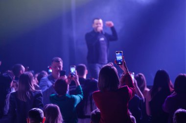 Seyirciler canlı ışıklandırmalı bir müzik etkinliğinde telefonlarıyla canlı performans kaydediyorlar..