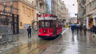İstanbul, Türkiye - 12 Nisan 2025: Tipik kırmızı tramvay, elinde şemsiyelerle yağmurlu cadde boyunca ilerliyor
