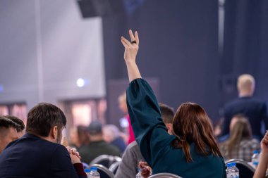 Kalabalık ortamdaki kişi, işaret vermek ya da soru sormak için elini kaldırıyor. Resmi bir toplantı veya konferans oturumuna katılım ve bağlılık vurgulandı.