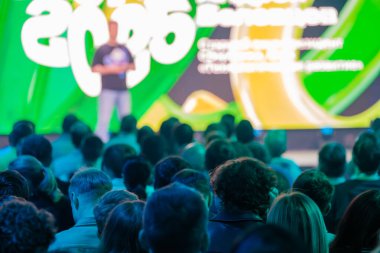 Çeşitli izleyicilerin dinamik renkli sunum ortamında yer aldığı parlak konferans sahnesi