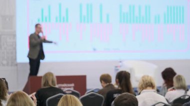 Profesyonel konferans veya seminer ortamında izleyicilere ekranda veri sunan konuşmacı.