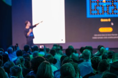 Seyirciler profesyonel bir konferansta dijital ekranla sunan bir konuşmacıyı dikkatle izliyorlar..