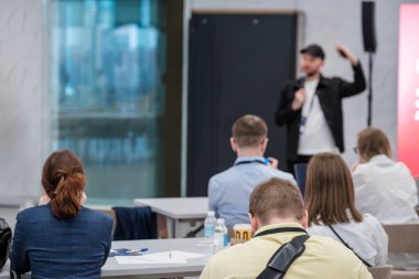 İzleyiciler kapalı alanda yapılan resmi bir iş sunumu sırasında konuşmacıyı dinliyor.