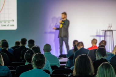 Seminerde izleyicilere görsel yardım ve grafiklerle hitap eden, etkileşimi vurgulayan ve öğrenen konuşmacı.