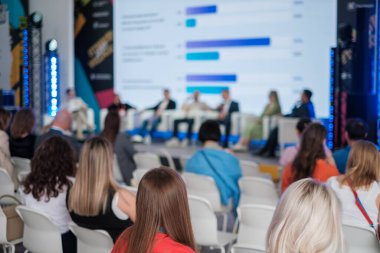 Profesyoneller bir iş konferansına katılıyor, seyirciler arasında sahnede sunumlar yapılıyor..