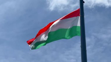 Açık mavi gökyüzünde dalgalanan kırmızı, beyaz ve yeşil çizgili Macar ulusal bayrağı.