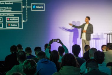 Bir iş etkinliği sırasında izleyicilerin dikkatle izlediği ve kaydettiği sahnede konuşmacı