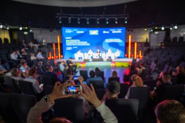 Akıllı telefonlara odaklanan bulanık izleyiciler ana sahnede canlı panel tartışmasını kaydediyor.