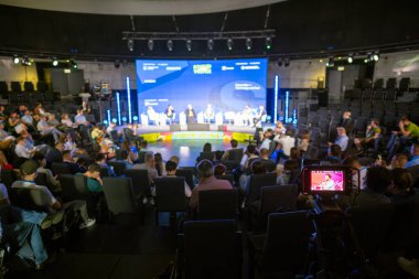 Katılımcıların sahnede bir panel tartışmasını izlediği modern bir mekanda konferans