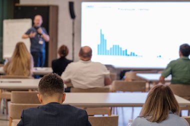 Konferans ortamında sunumu izleyen katılımcılar hoparlör ve görsel verilere odaklandı