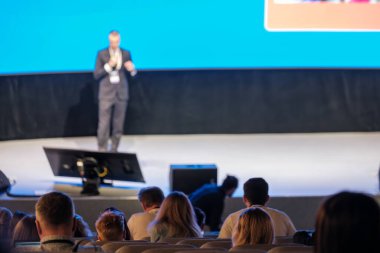 Konferans konuşmacısı seyircilere mavi ekran sunuyor. Konferans salonunda profesyonel atmosfer.