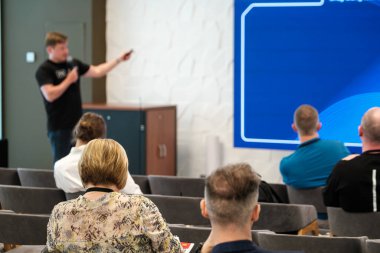 Sunucu, bir ofis ortamındaki seminerde oturan katılımcılarla görüşlerini paylaşıyor