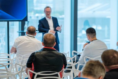 Modern, parlak konferans odasında geniş pencereli izleyicilere sunum yapan konuşmacı.