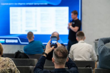 Konferans sırasında sunucuyu mavi dijital arkaplan odaklı akıllı telefon ekranında yakalar.