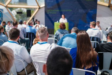 İnsanlar açık havada oturmuş konferansta profesyonel bir konuşmacıyı dikkatle dinliyor..