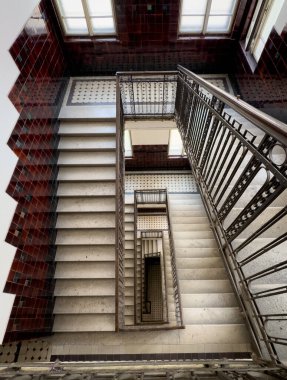 Merdiven döşemelerine, korkuluklara ve sıcak ışıklandırılmış iç manzaraya bakıyorum..