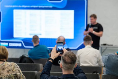 Adam sunucu konuşurken akıllı telefon ekranında seminer slaytını yakalıyor. Eğitim ve mesleki atmosfer.