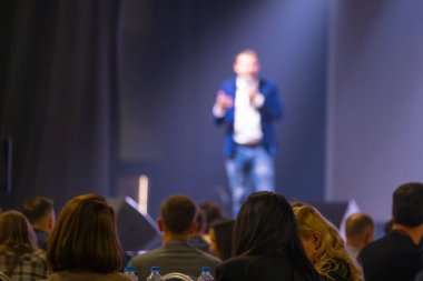 Bulanık konuşmacı konferansta ön plandaki katılımcılara odaklanmış bir şekilde izleyiciye hitap ediyor.