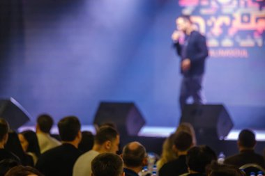 Halka açık konuşma etkinliği arka planda ilgili izleyicileri ve bulanık sunucuyu gösteriyor.