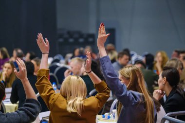 Kalabalık bir iş toplantısına el kaldırarak aktif olarak katılan bireyler.