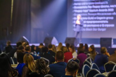 Konferansa katılan iş adamları, iyi aydınlatılmış bir sahnede sunumları dinliyorlar.